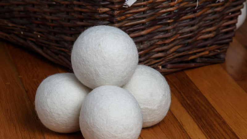 Four wool dryer balls in front of  wooden basket—How to store wool dryer balls